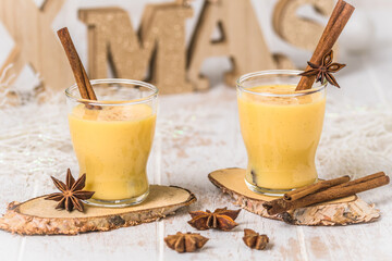 Two glaTwo glasses of eggnogg with cinnamon sticks on white wooden background, christmas. Auld...