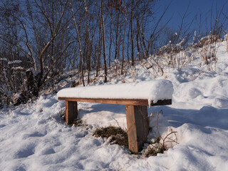 a bench in the park is covered with snow. a wooden bench is covered with snow. winter sunny day in the park. a snow-covered bench against a blue sky.