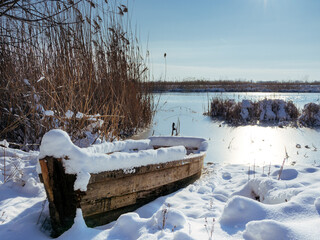 a wooden boat covered with snow on the background of a frozen river. winter river is covered with snow. ice on the river. old boat fucking river covered with snow.