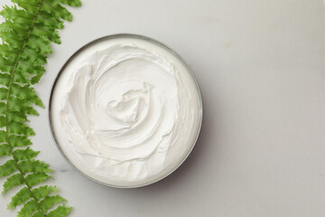 Jar of face cream and green plant on white marble table, flat lay. Space for text