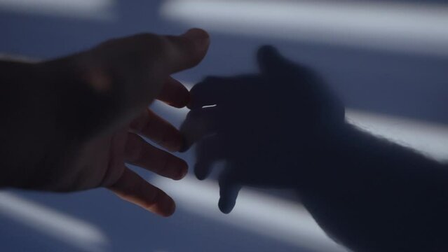 Dramatic looking shadows from window blinds cast on wall as hand touching it. Male hand passes over a wall with hard shadows from shutters or bars. Blue and dark scene. Poetic slow movement in room