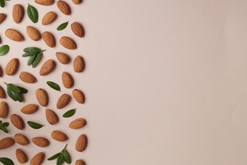 Delicious almonds and fresh leaves on beige background, flat lay. Space for text