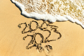 A wave on a sandy beach washes away the inscription 2022-2023