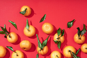 Fresh ripe small tangerines with leaves lie on a wooden plate. Red festive fruit background. Happy...