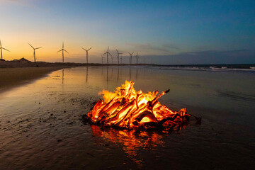 Fogueira acesa na praia e torre de energia eólica, em Icaraí Ceará - obrazy, fototapety, plakaty
