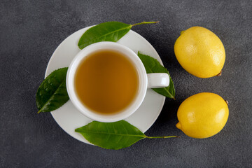 A cup of green tea, tea leaves and lemons, on dark background
