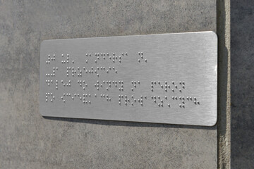 Silver plate with Braille text on grey wall, closeup