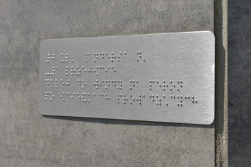 Silver plate with Braille text on grey wall, closeup