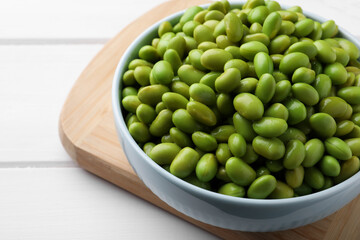Bowl of delicious edamame beans on white wooden table, closeup