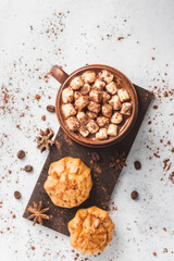 Hot chocolate drink with marshmallows in a cup and sweet bakery eclair dessert sprinkled with cocoa powder, cinnamon stick and star anise, top view