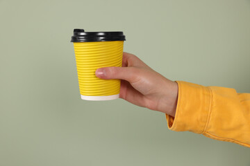 Woman holding takeaway cup with drink on pale green background, closeup. Coffee to go