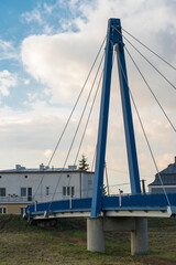 Wiszący most dla pieszych . Przęsło wiszące na stalowych linach . Pylon mostu na tle nieba niebieskiego  z chmurami białymi . © Grzegorz