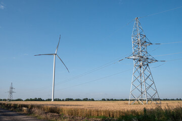 Windmill produces energy. Wind turbine supports row of power transmission lines with renewable and...