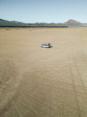 Obraz premium Aerial view of self converted camper van recreational vehicle driving on a dry lake bed in the desert of southern nevada United States with solar panels and bikes mounted to the rv van life rig.
