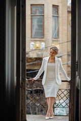 a beautiful, confident woman in a white suit on the balcony of the old building.