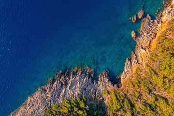 Aerial top view of clear blue water sea, rocks and forest at sunset in summer Turkey