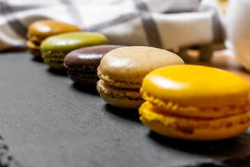 Green, yellow, chocolate and brown macarons served on a slate over a wooden table with decorative cloth and newspaper