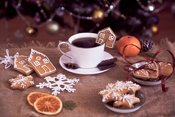 Aesthetics Christmas breakfast. Ginger cookies of cute homes and snowflakes and cup of coffee near Christmas tree.