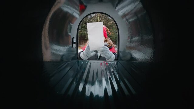 POV Cute little kid boy puts a letter with his Christmas wishes addressed to Santa Claus, Notrh Pole into the mailbox