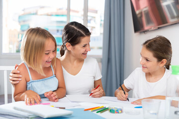 Two little girls with mother drawing together at home