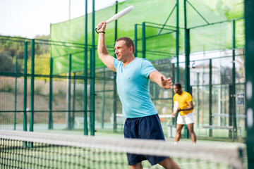 Obraz premium Caucasian man in sportswear playing padel tennis match during training on court.