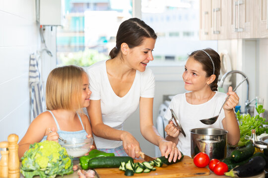 Woman With Two Kids Cooking Together Cutting Vegetables For Soup And Salad At Home Kitchen