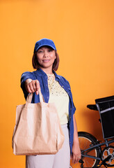 Restaurant delivery employee wearing blue uniform while delivering food order to customer during lunch time. Pizzeria worker standing in studio with yellow background. Takeout service concept