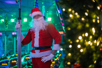 Portrait von einem verkleideten Weihnachtsmann, der auf einem Weihnachtsmarkt von bunten Lichtern...