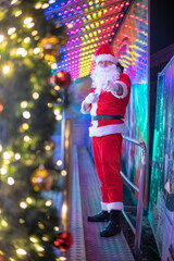 Portrait von einem verkleideten Weihnachtsmann, der auf einem Weihnachtsmarkt von Bokeh von bunten...