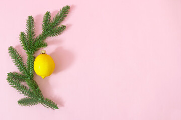 Pine tree branches with a fresh lemon as Christmas decoration against pink background. Minimal surreal design for season greetings card or banner. Flat lay.
