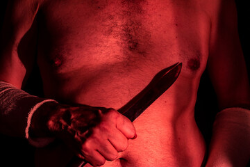 Knife attack concept. Killer, shirtless, is attacking with knife with drops of red fake blood.