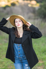 Girl in black coat and jeans holding her straw hat