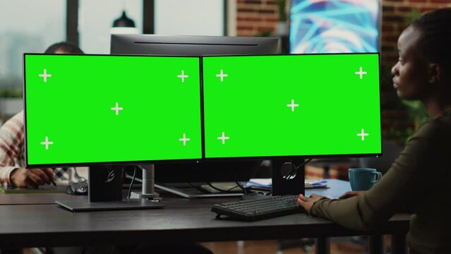 Young digital creator looking at computers with greenscreen, working on professional monitor with isolated display. Woman 3d editor analyzing blank chroma key mockup copyspace.