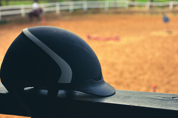 Close up view of  black Equestrian helmet with blurred horse farm view. Isolated Horse riding hat on the railing in the horse farm.