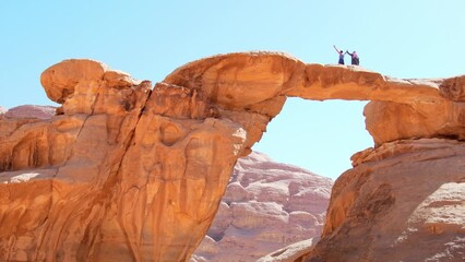 Arab bedouin guide with tourist stand pose on famous arch bridge in wadi rum desert pose and enjoy panoramic view of scenic rock formations