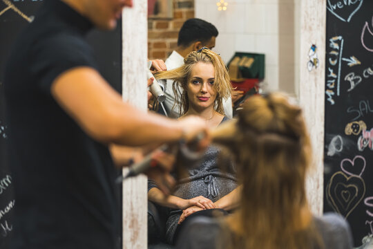 Rear mirror view of male hairdresser blowdrying long wet hair of a woman. High quality photo