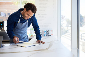 Smiling male cafe owner analyzing accounts book on checkout counter