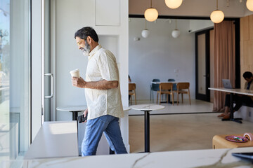 Smiling mature man with disposable coffee cup leaving coffee shop