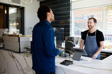 Smiling male owner talking to customer in coffee shop