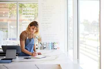 Female owner writing in book while analyzing accounts at cafe