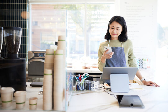 Smiling female cashier using mobile phone at in coffee shop