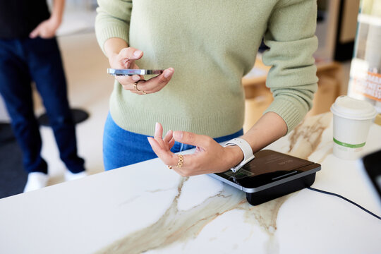 Midsection of female customer scanning smart watch on POS system