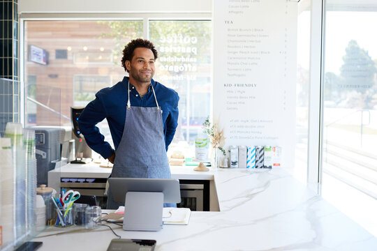 Smiling male owner wearing apron while contemplating in coffee shop