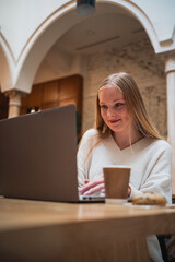 Smiling girl using her laptop and looking at it. She is working at a coffee shop.