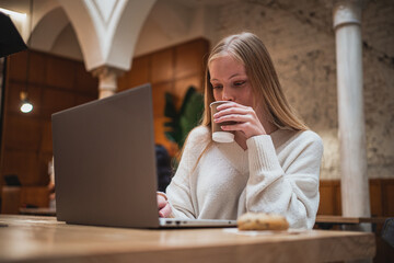 Relaxed girl drinking coffee while is using her laptop to study for a exam.