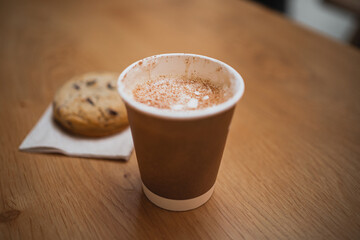 Close up shot of cup of hot cappuccino with a chocolate cookie on a table of a coffee shop