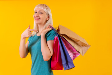Fototapeta na wymiar Pointing to shopping bags on sale, blonde caucasian girl in studio on yellow background