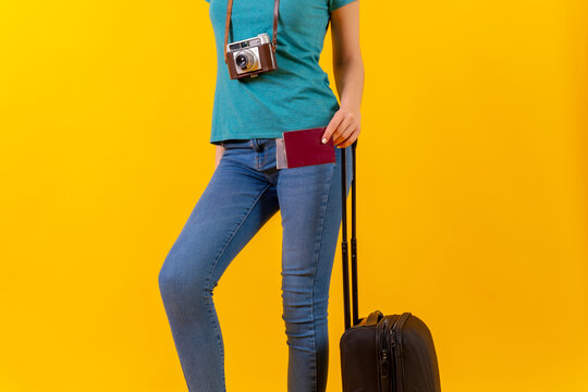 unrecognizable person tourist with suitcase and passport, studio yellow background