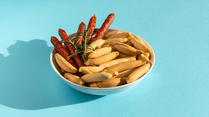 Sticks of Chorizo and picos bread sticks in bowl on the blue background with hard shadow