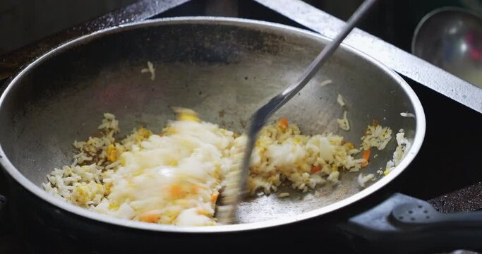 Close-up of a chef cooking fried rice in a hot wok on the stove.